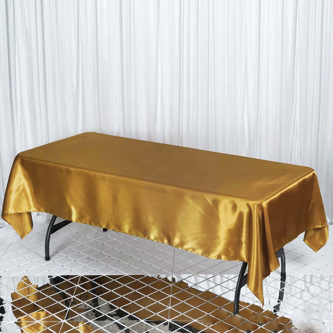 Gold satin tablecloth on a sleek table with a mirrored surface.