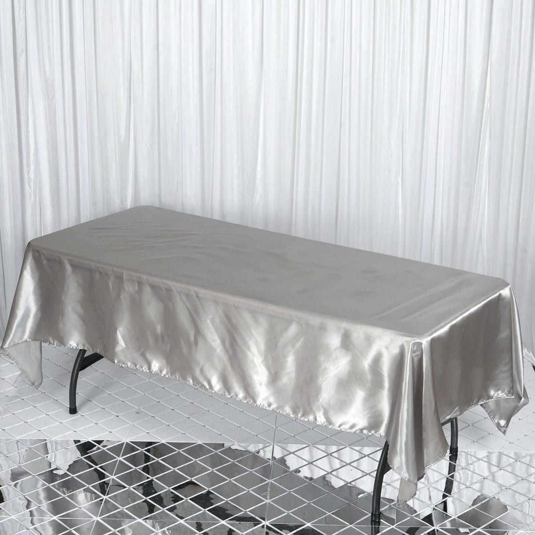 Silver satin tablecloth draped over a table in a studio setting.