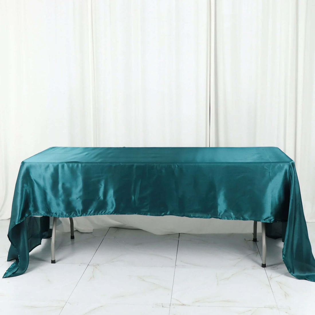 Teal satin tablecloth draped over a table in a studio setting.