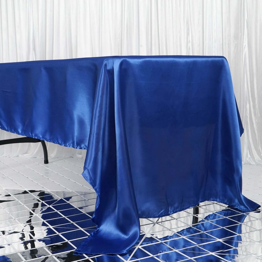 Blue satin tablecloth on a table against a draped backdrop.