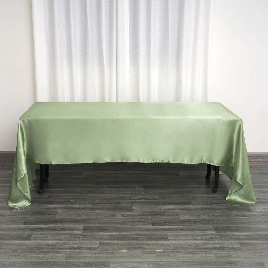 Green satin tablecloth on a wooden table with a white curtain backdrop.
