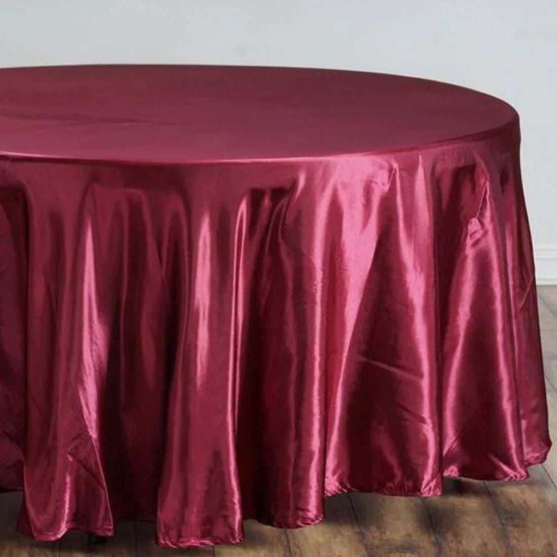 Burgundy round tablecloth on a wooden floor.