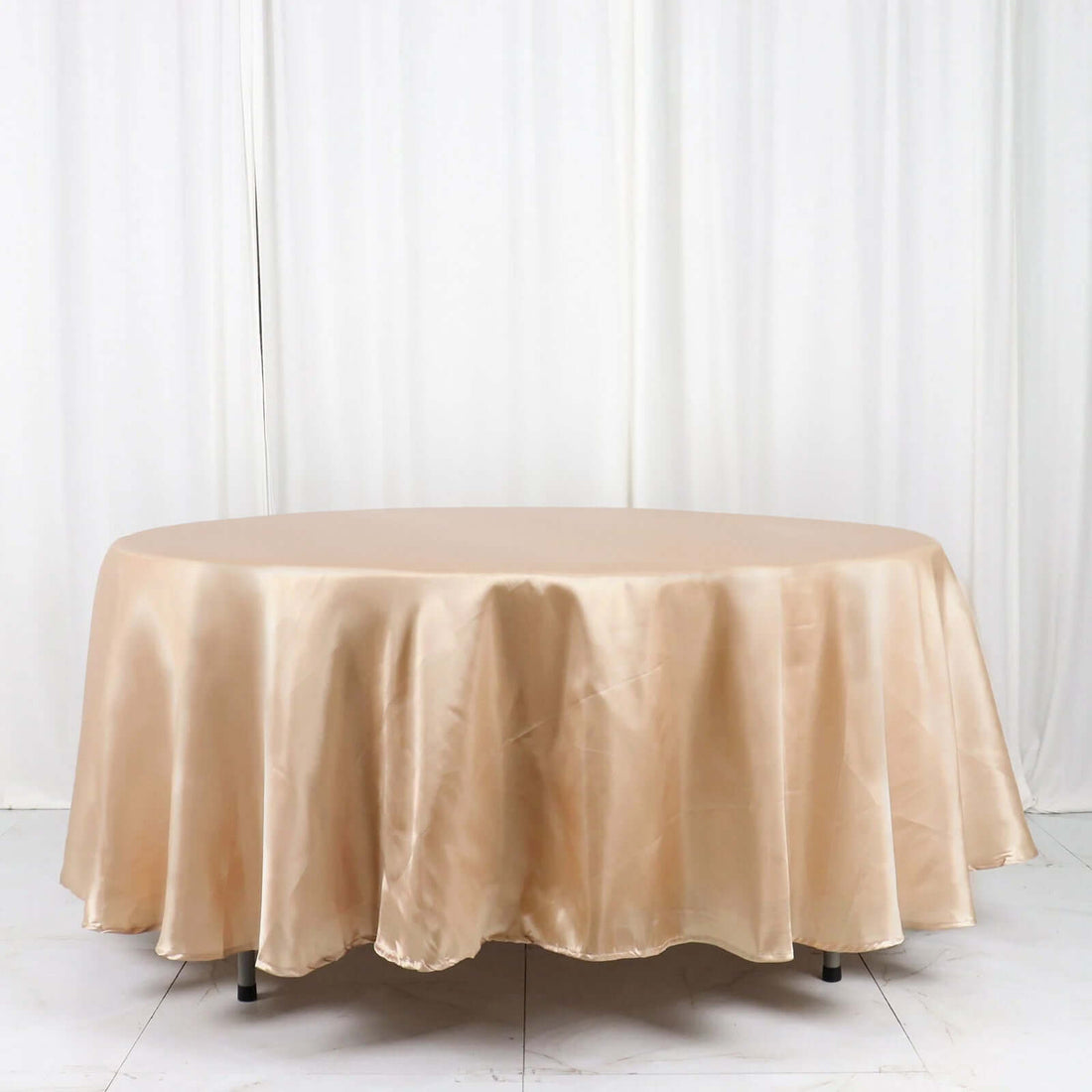 Beige satin tablecloth on a round table against a plain white backdrop