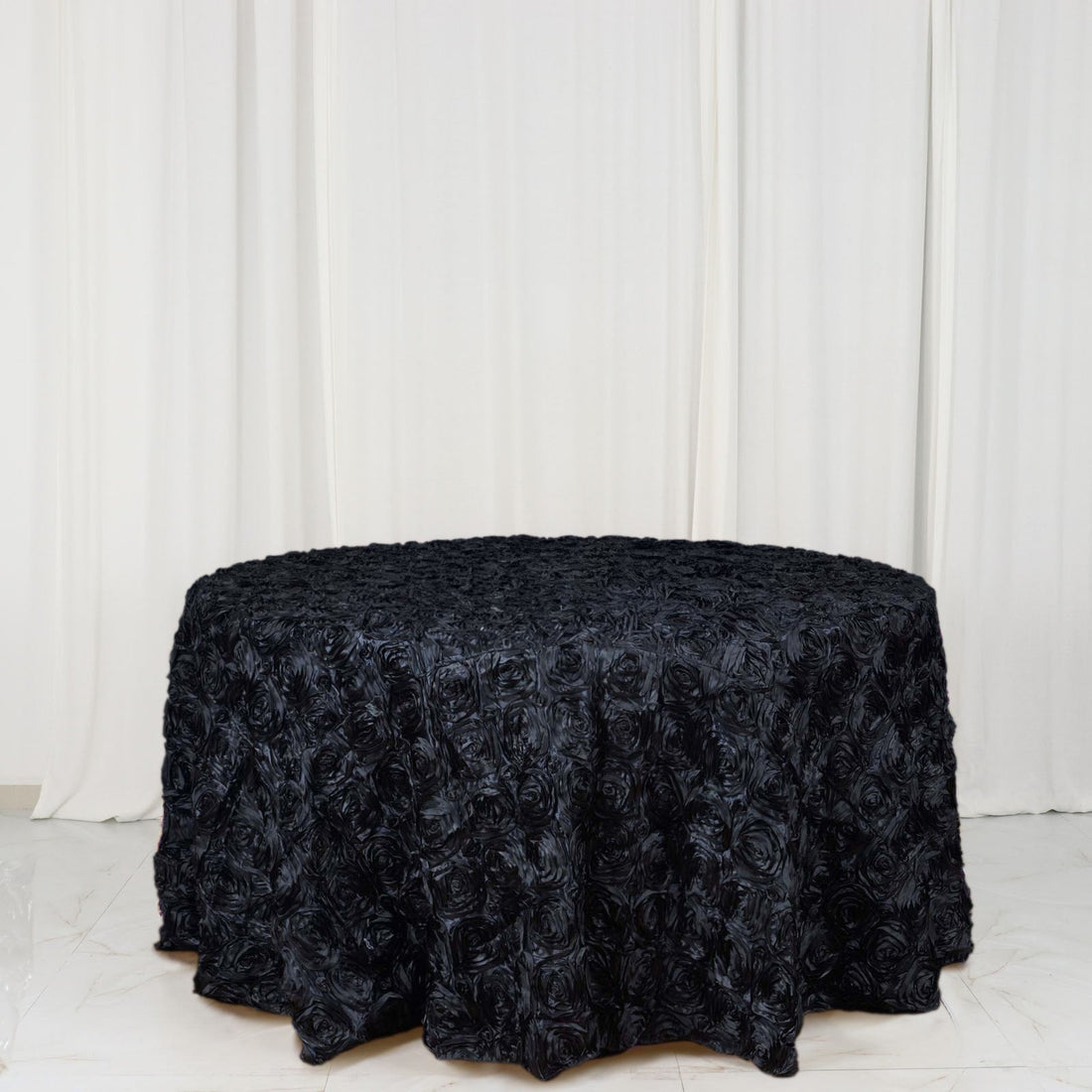 Black rose-patterned tablecloth on a round table against a white backdrop.