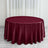 Burgundy round tablecloth on a wooden floor with white curtains in the background.