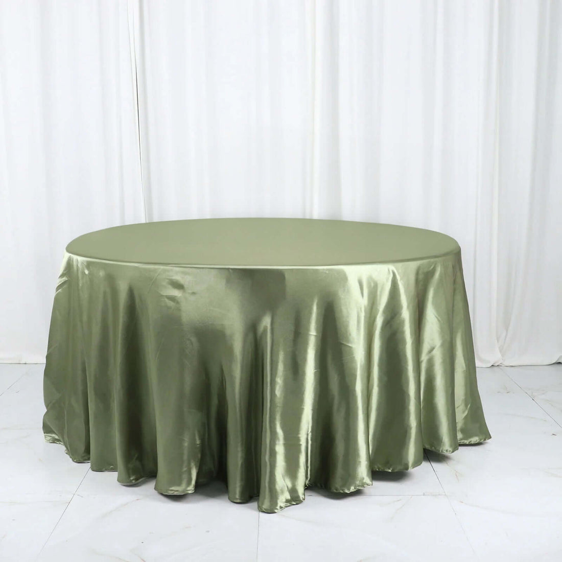 Olive green satin tablecloth on a round table against a plain backdrop