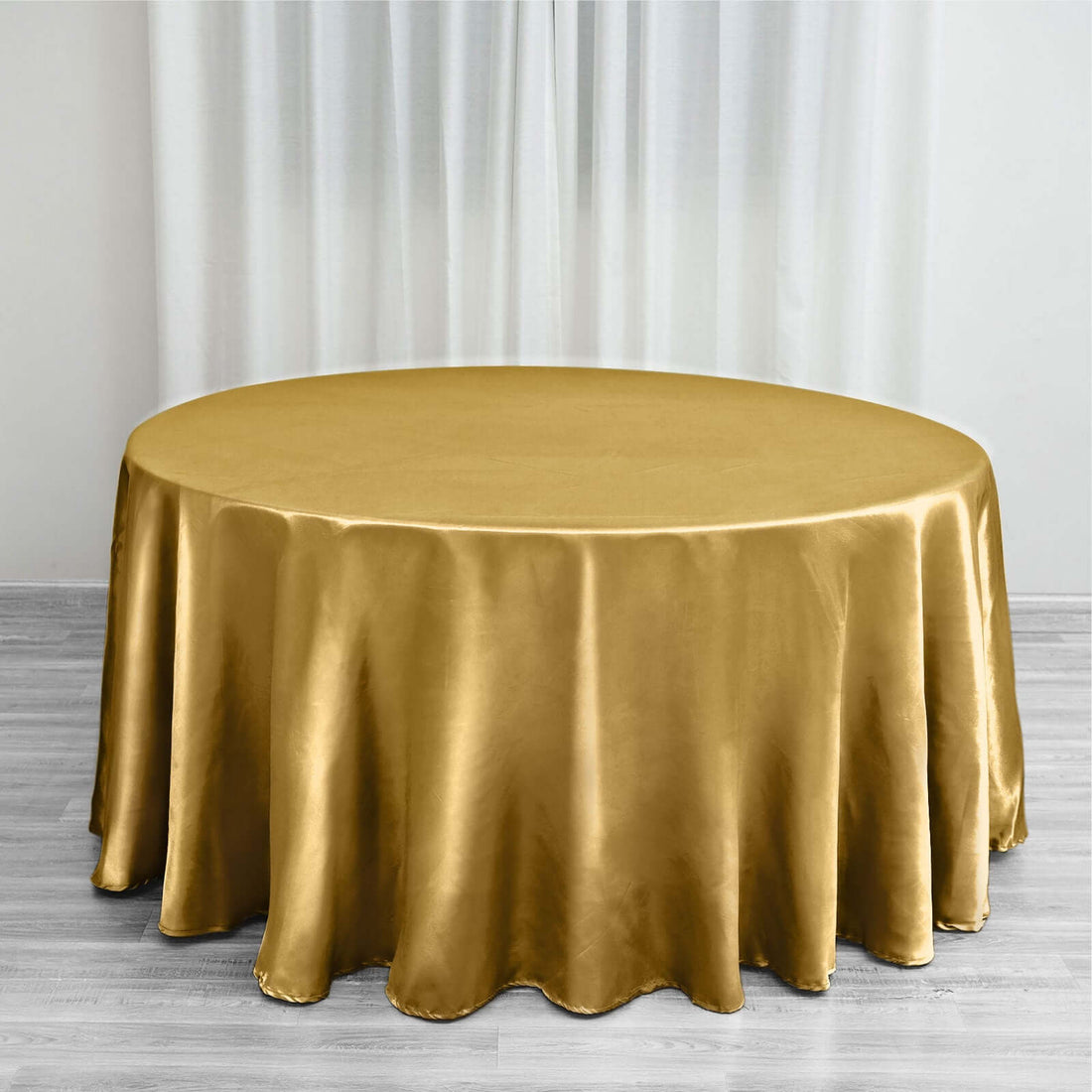 Gold satin round tablecloth on a wooden floor with sheer curtains.