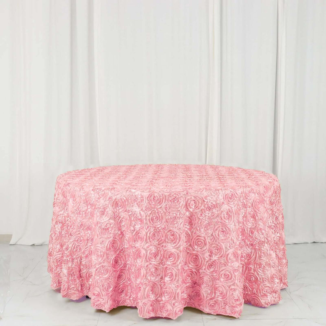 Pink rose-patterned tablecloth on a round table against a white backdrop.