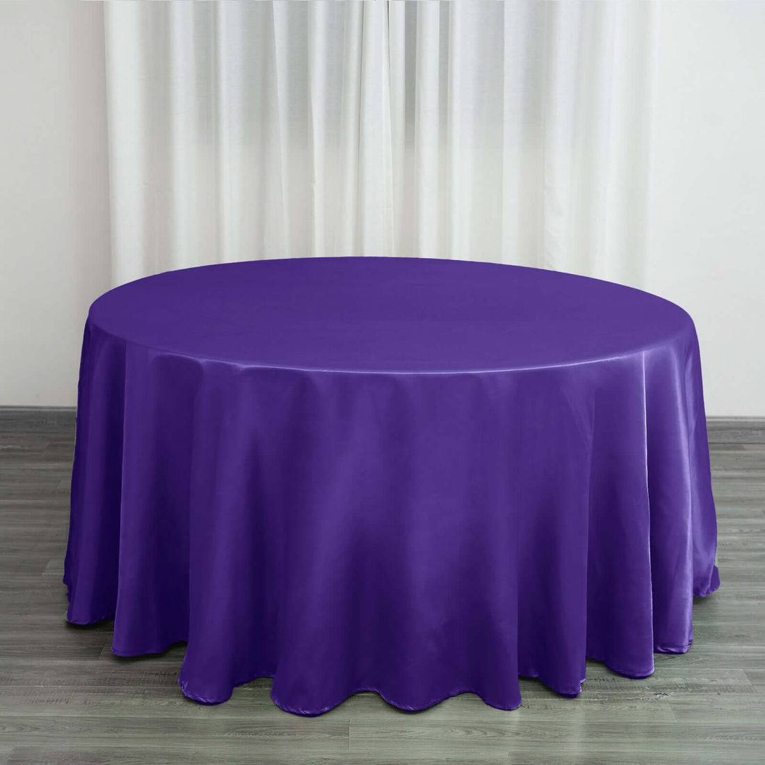 Purple round tablecloth on a wooden floor with curtains in the background.