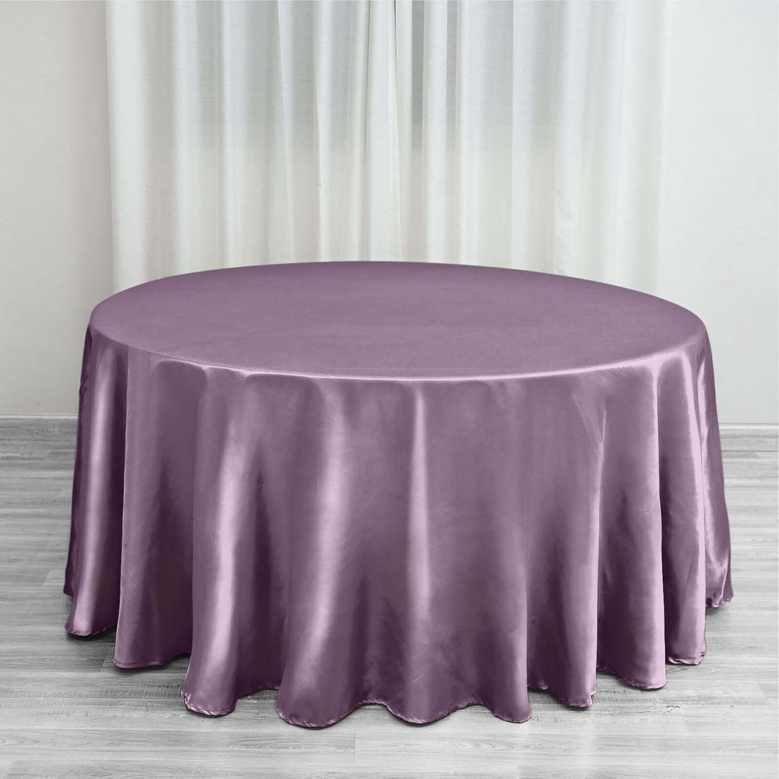 Purple satin round tablecloth on a wooden floor with curtains in the background.