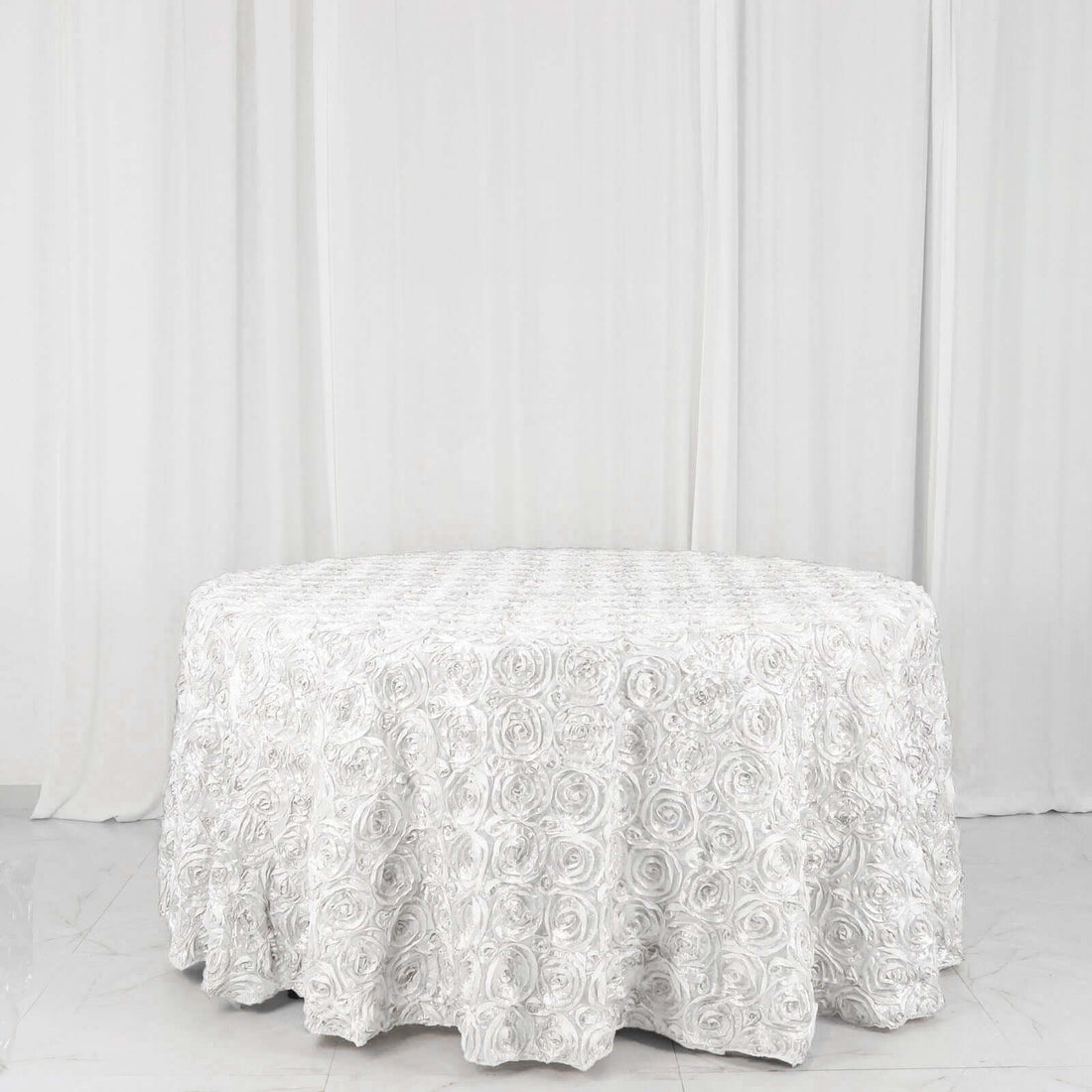 Round white rose-patterned tablecloth on a plain backdrop.