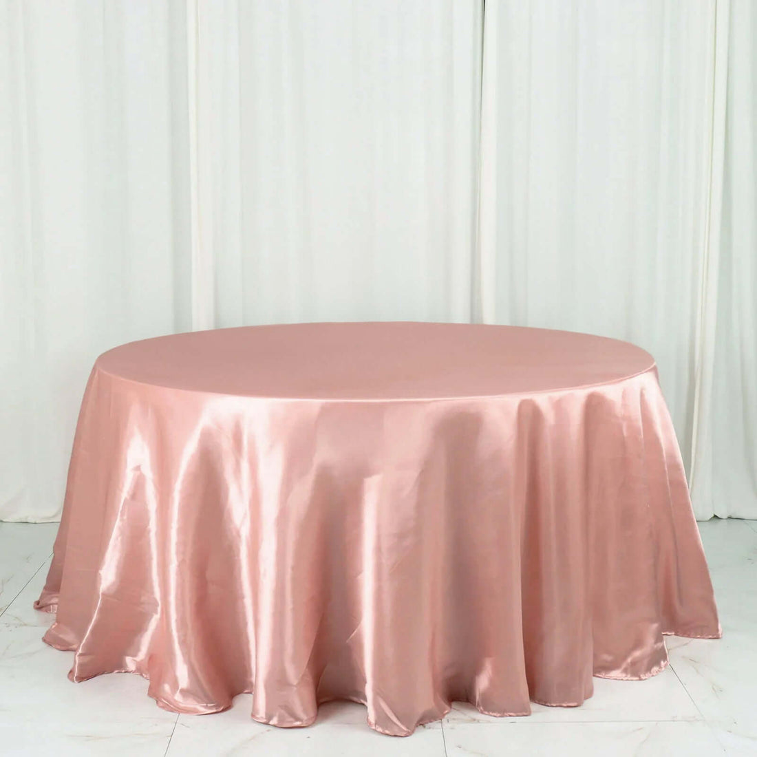 Pink satin round tablecloth on a plain backdrop.