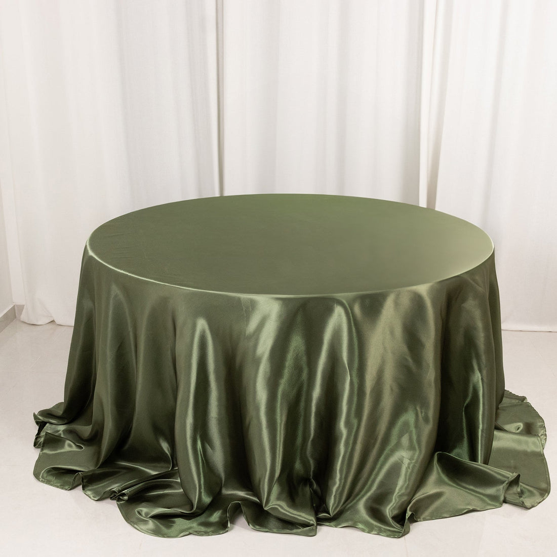 Green satin tablecloth on a round table against a plain backdrop.
