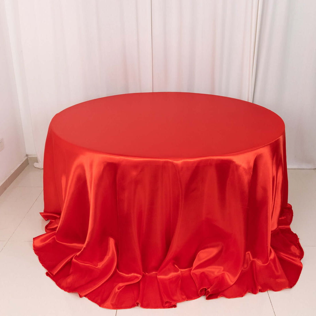 Red round tablecloth with elegant draping and a glossy finish.