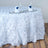 White rose-patterned tablecloth draping a round table with elegant dinnerware.
