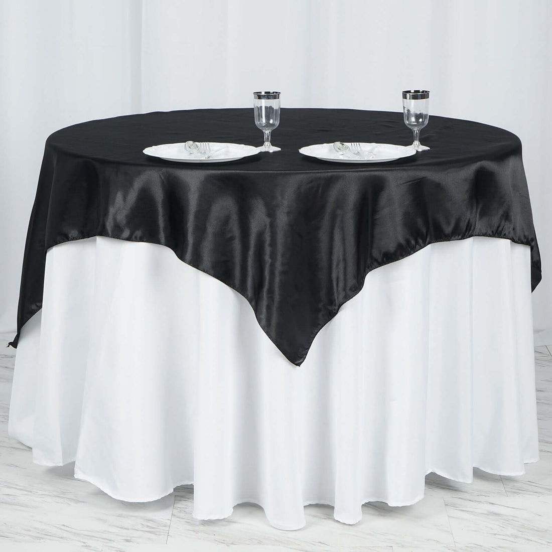 Black satin tablecloth draped elegantly over a round table with plates and glasses.