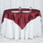 Round table set with burgundy satin tablecloth and white dinnerware on a white backdrop.