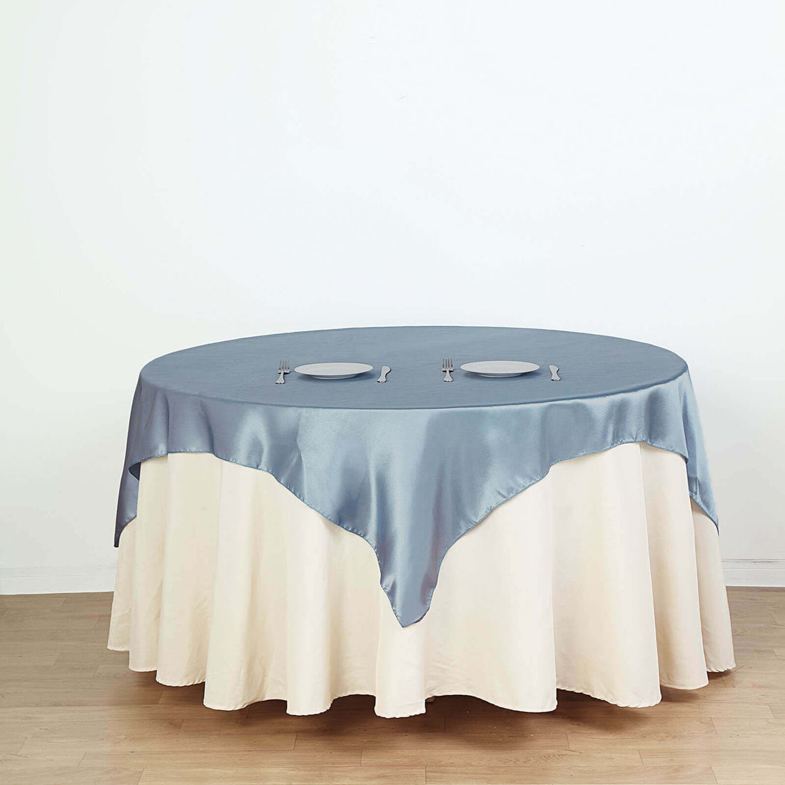 Round table with blue satin tablecloth and white skirt, set for dining.