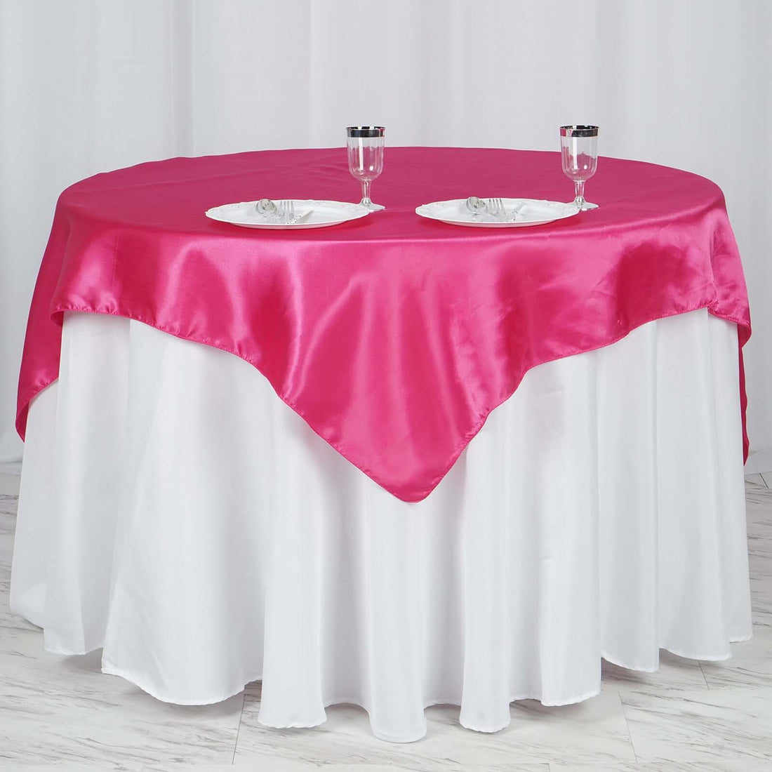 Pink satin table cover draped over a white table with plates and glasses.