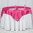 Pink satin table cover draped over a white table with plates and glasses.