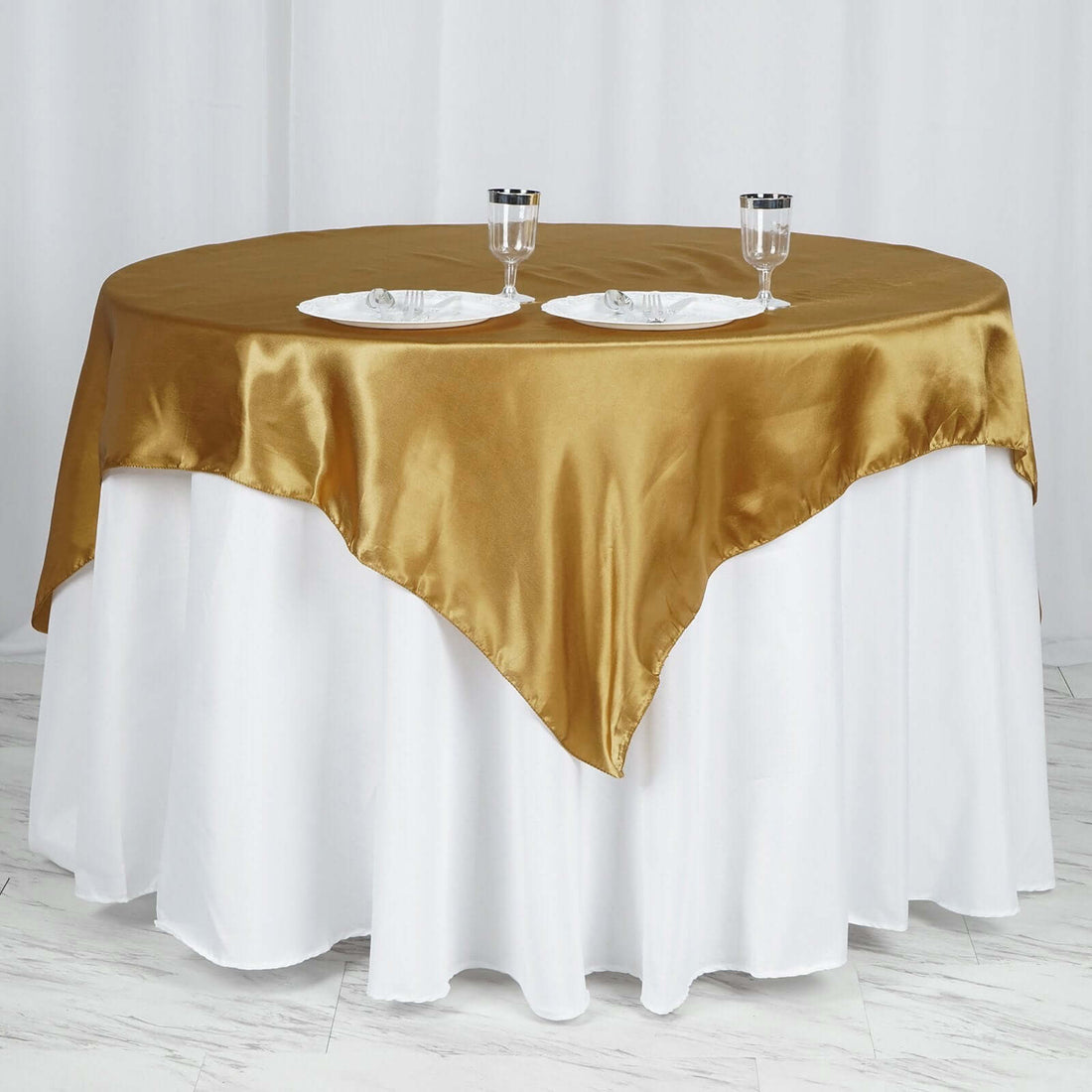 Gold satin tablecloth draped elegantly on a round table with plates and glasses.