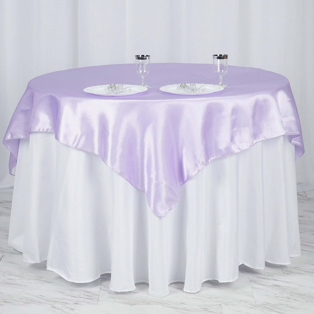 Purple satin tablecloth draped over a round table with white skirt.