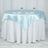 Round table with blue satin tablecloth and white overlay, set for two.
