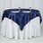 Navy satin tablecloth draped over a round table with white skirt and two plates