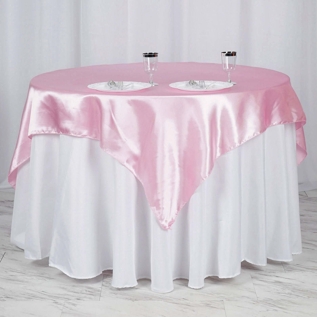 Round table with pink satin tablecloth and white overlay, set for dining.