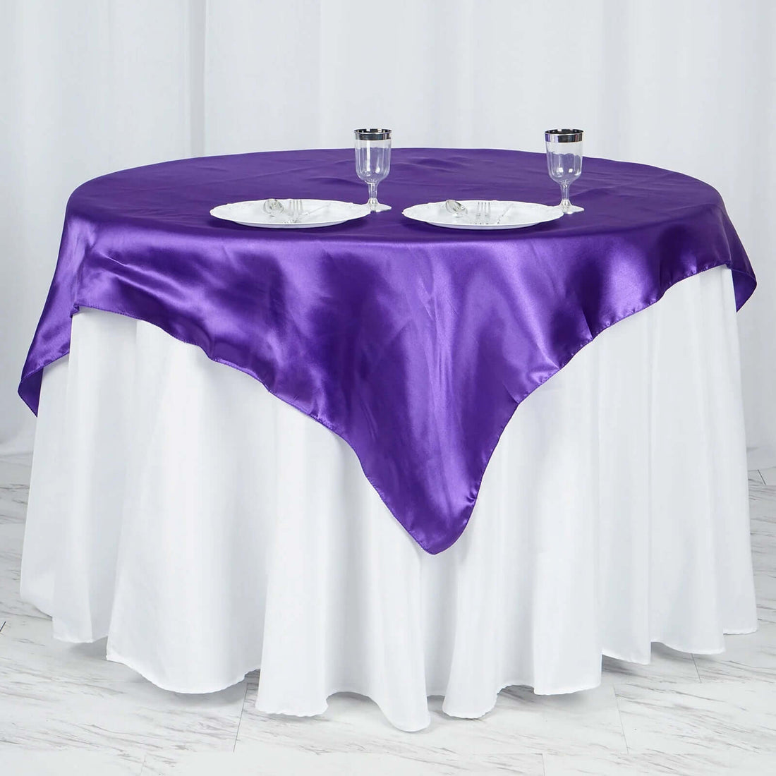 Round table with a purple satin tablecloth and two plates