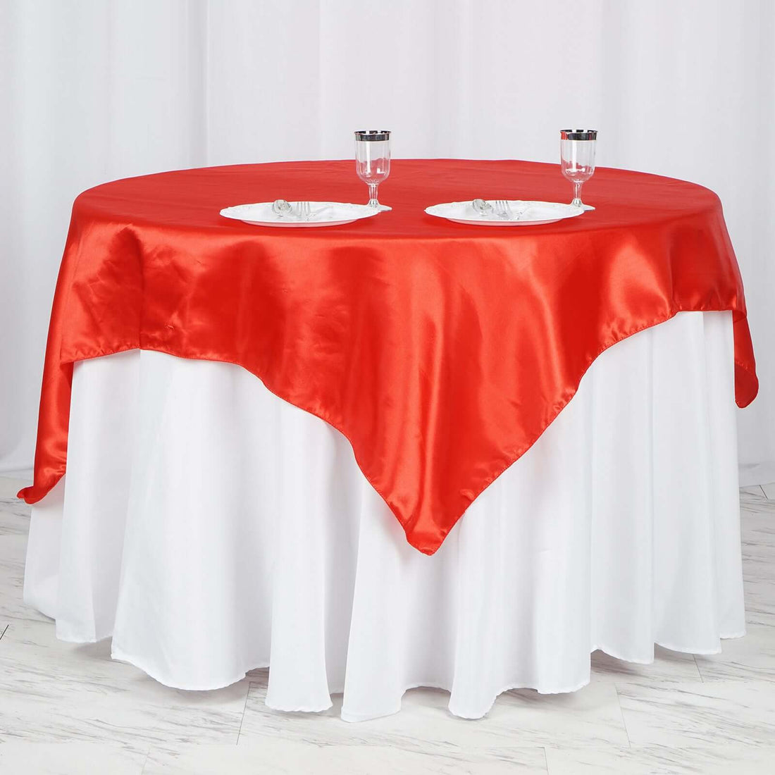 Red satin tablecloth on a round table with white skirt and plates.