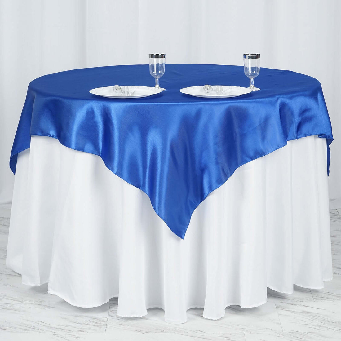Blue satin tablecloth draped over a white table with plates and glasses.