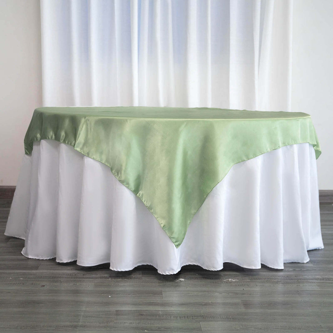 Green satin tablecloth draped over a white table skirt in a studio setting.
