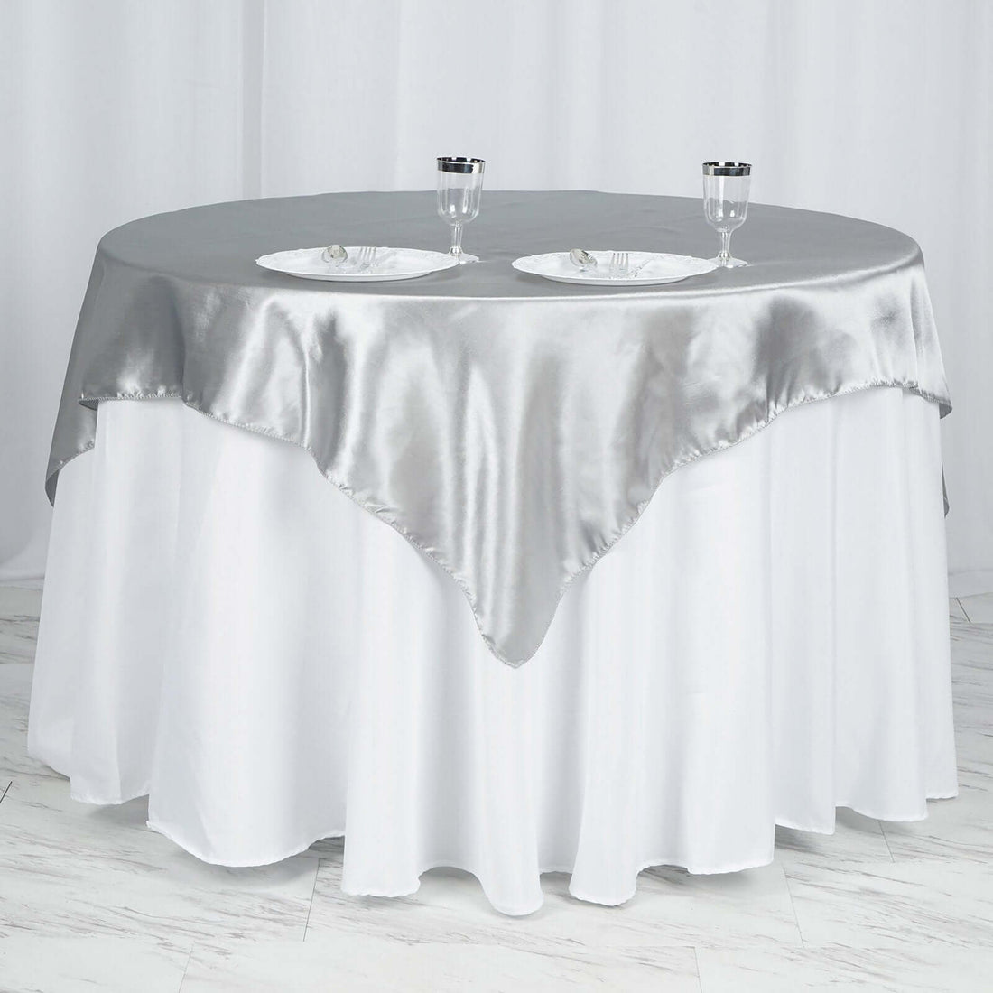 Silver satin tablecloth draped over a round table with glassware.