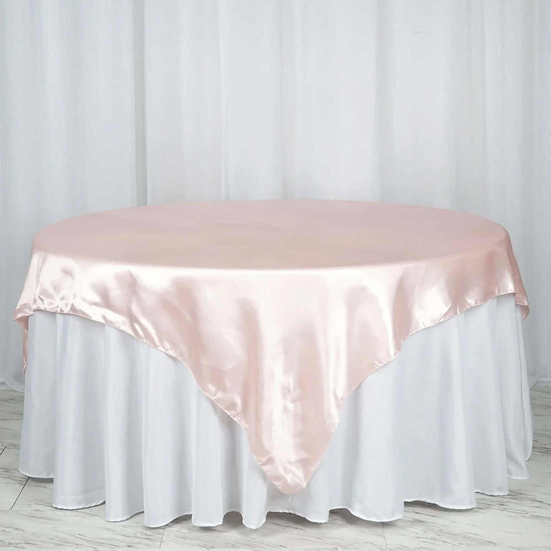 Pink satin tablecloth draped over a round table with a white skirt.