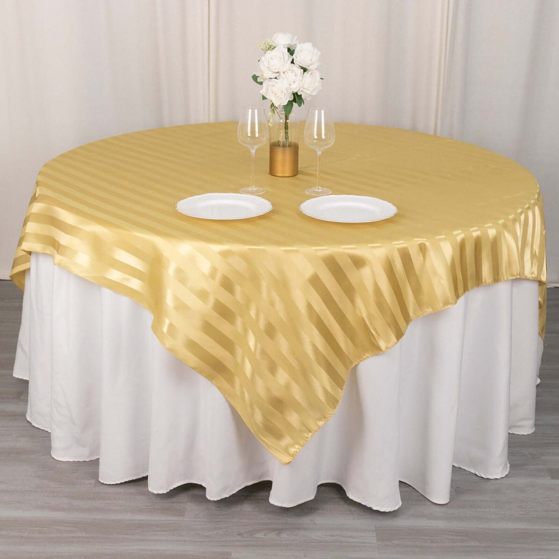 Gold striped round tablecloth on a dining table with plates and flowers.