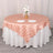 Round peach satin tablecloth draped over a table with white plates and flowers.