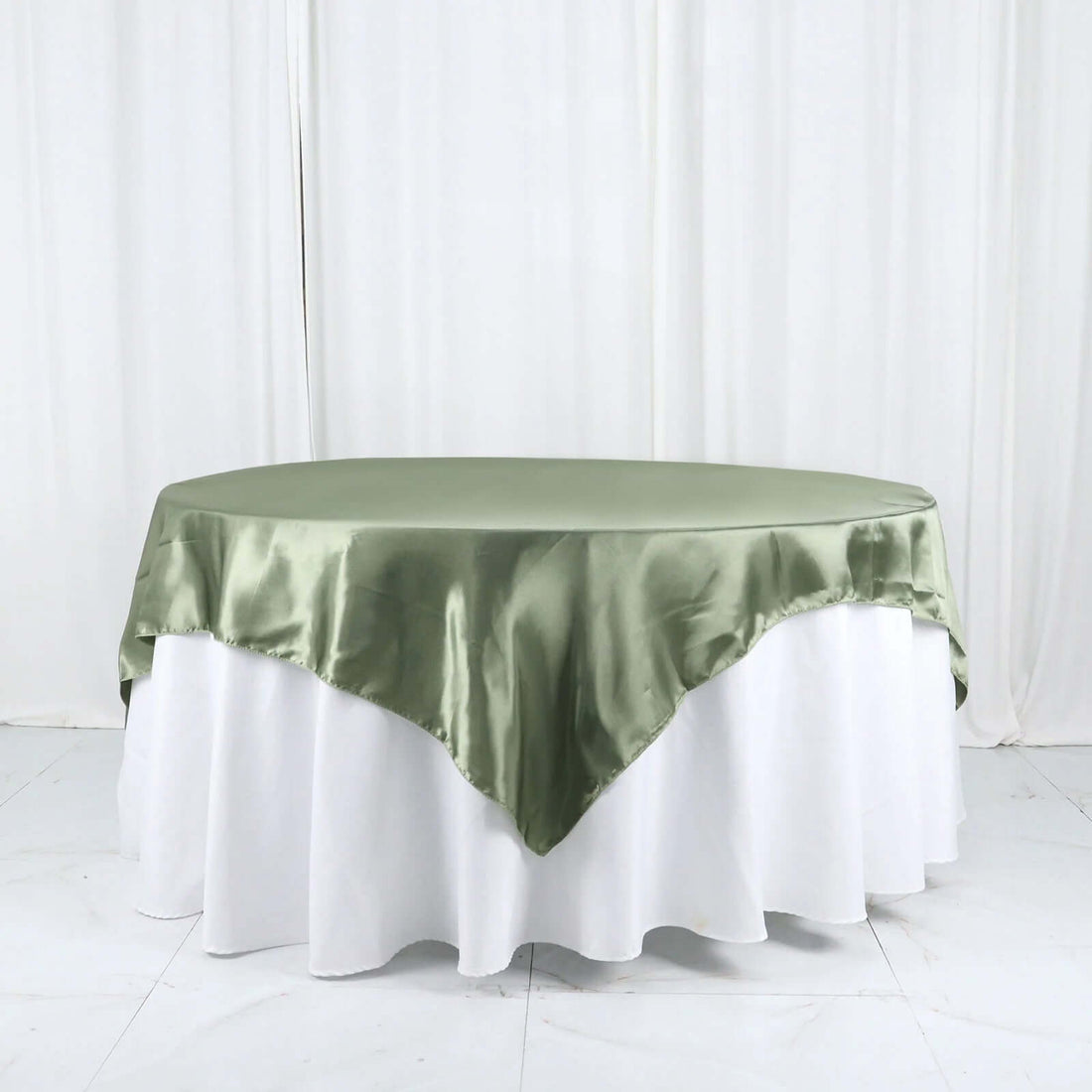 Green satin tablecloth draped over a round table in a studio setting.