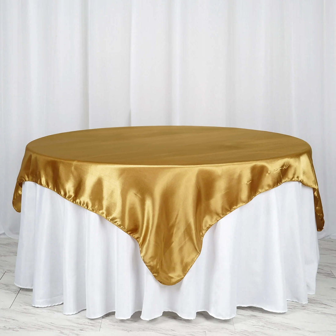 Gold satin tablecloth draped over a round table with a white skirt.