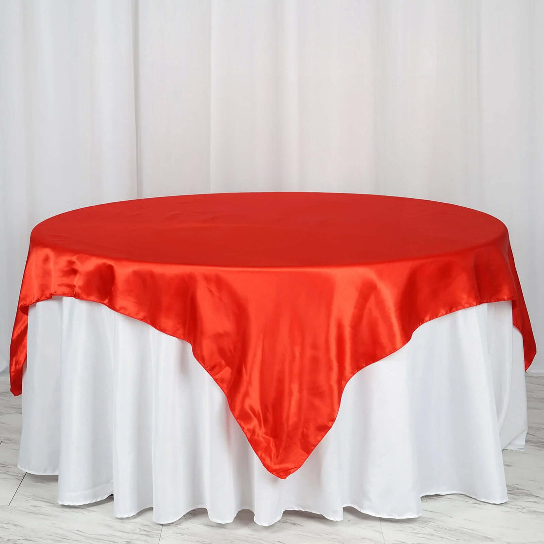 Red satin tablecloth draped over a round table with white skirt.