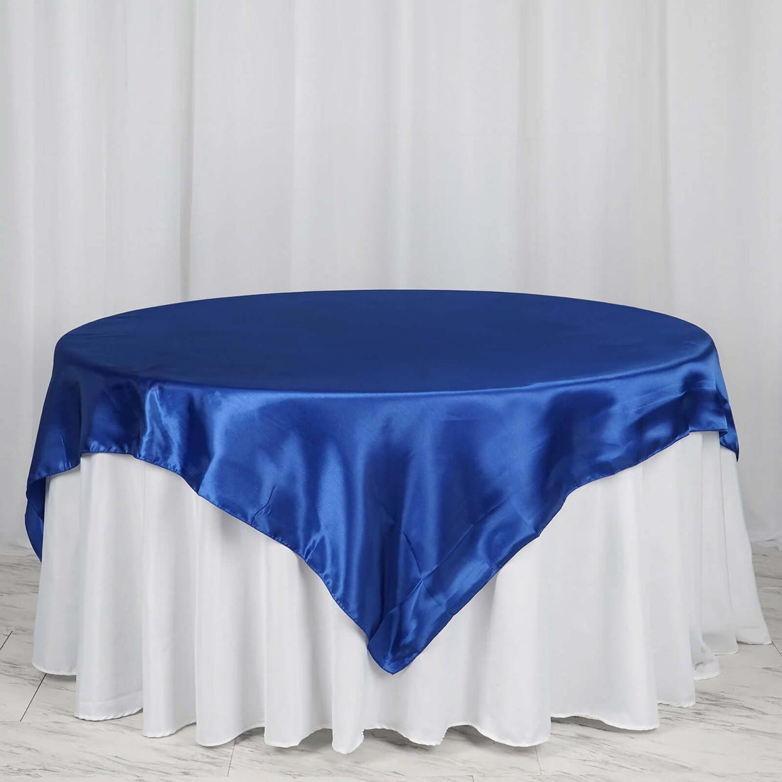 Blue satin tablecloth draped over a round table with white skirt