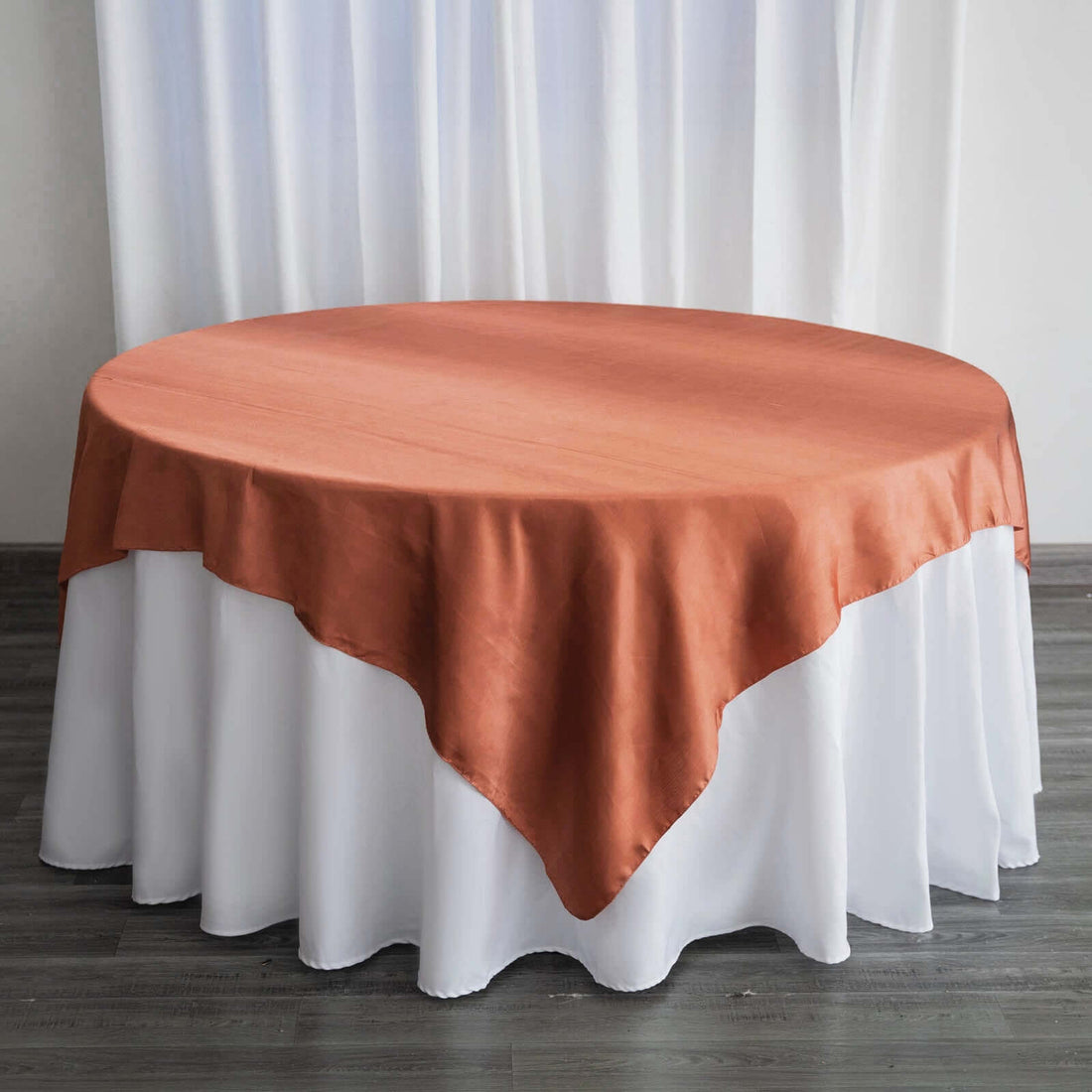 Round table with a rust-colored tablecloth and white skirt.