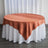 Round table with a rust-colored tablecloth and white skirt.