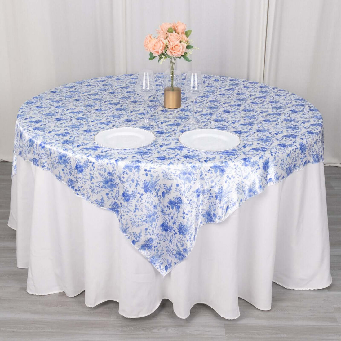 Blue floral tablecloth on a round table with plates and flowers.