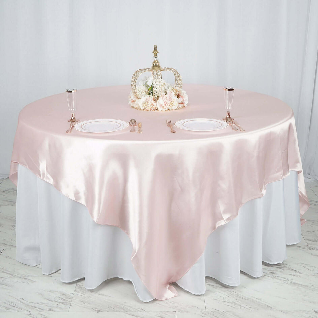 Elegant round table set with pink satin tablecloth and floral centerpiece.