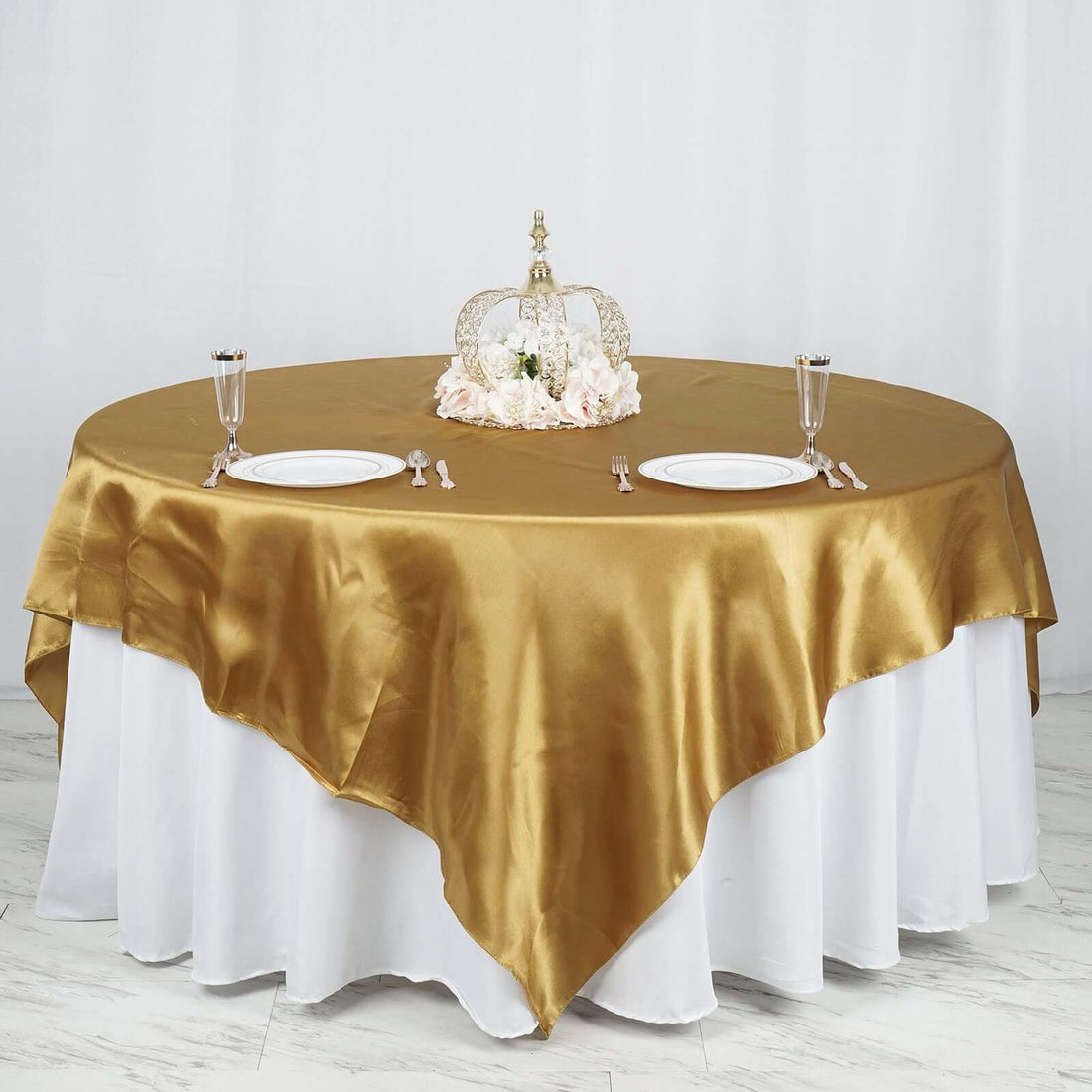 Elegant round table set with gold satin tablecloth and decorative centerpiece.