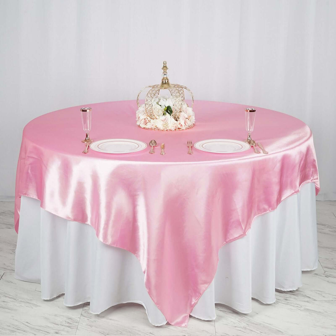 Elegant round table set with pink satin tablecloth and floral centerpiece.
