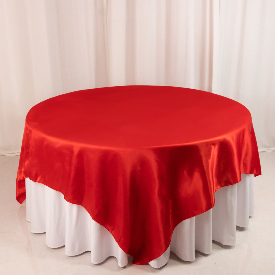 Red satin tablecloth draped over a round table.