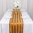 Gold striped table runner with white plates and floral centerpiece on a dining table.