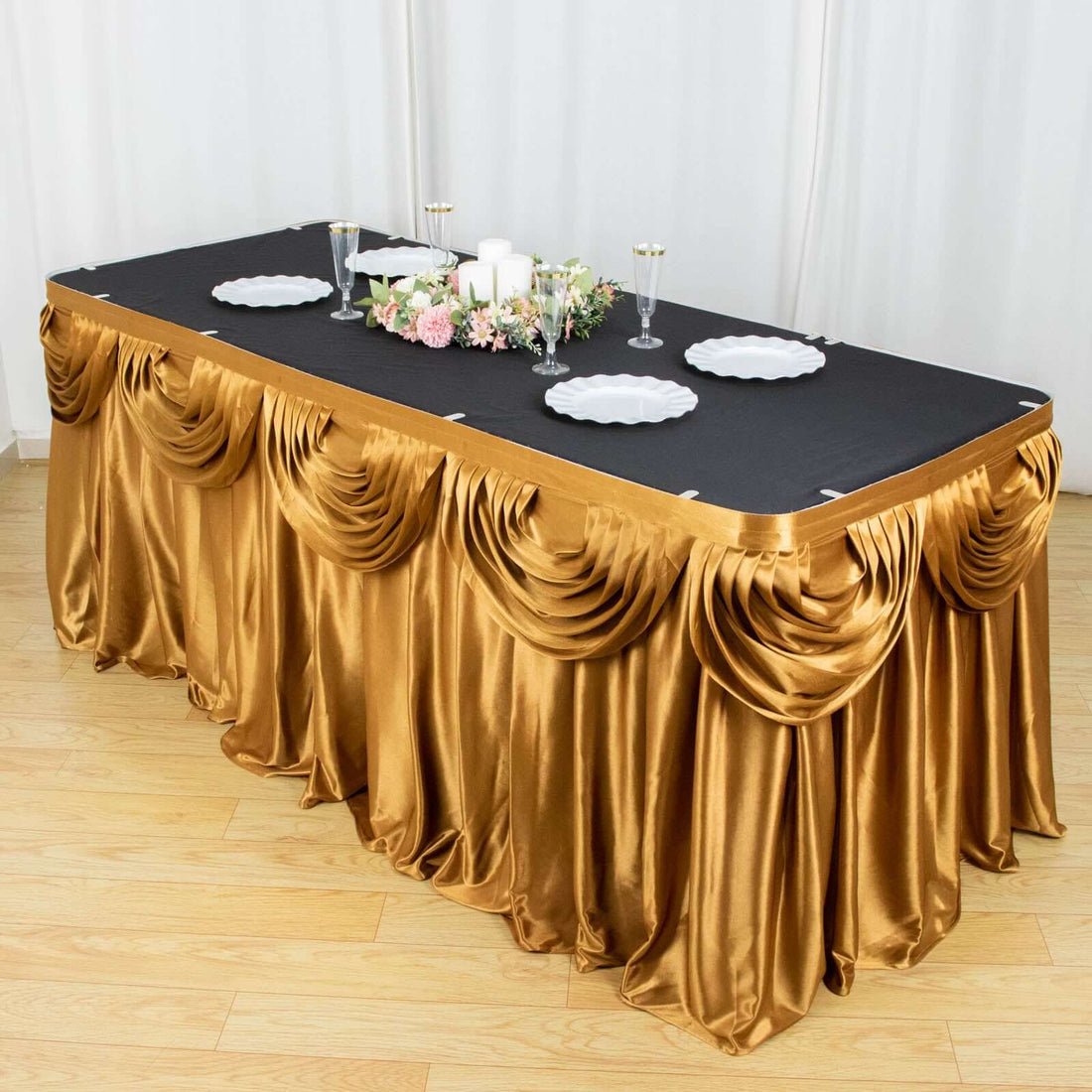 Elegant gold pleated table skirt draped over a black tablecloth with decorative accents.